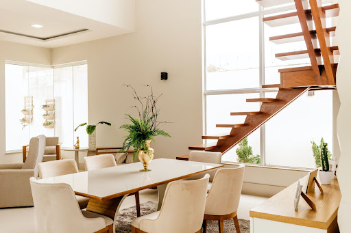 White living room with a wooden, floating staircase, a six-person dining table, and bright light.