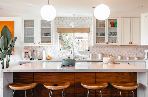Kitchen with hexagonal backsplash, four barstools, orange decor, and two hanging spherical lights.