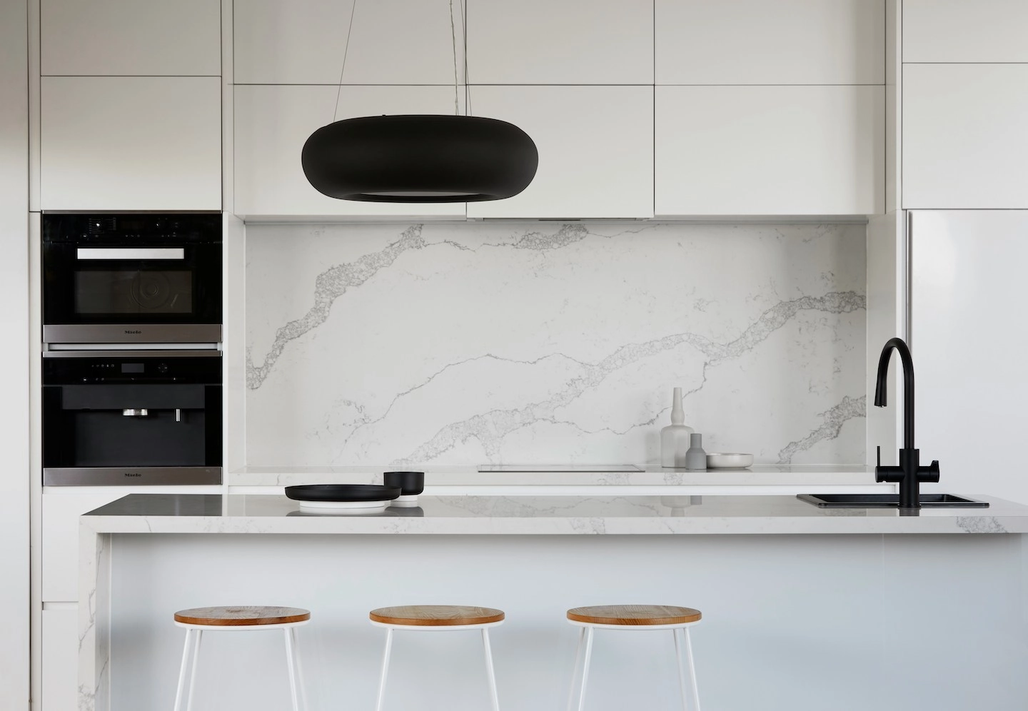 Kitchen with marble backsplash and countertop and three barstools.